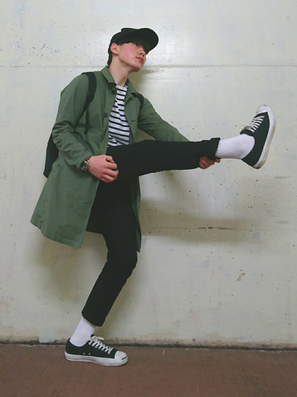 グリーン系のステンカラーコート、ブラック系のバックパック/リュック、ホワイト系のTシャツ/カットソーを着用したメンズの春コーディネートの1枚目の写真