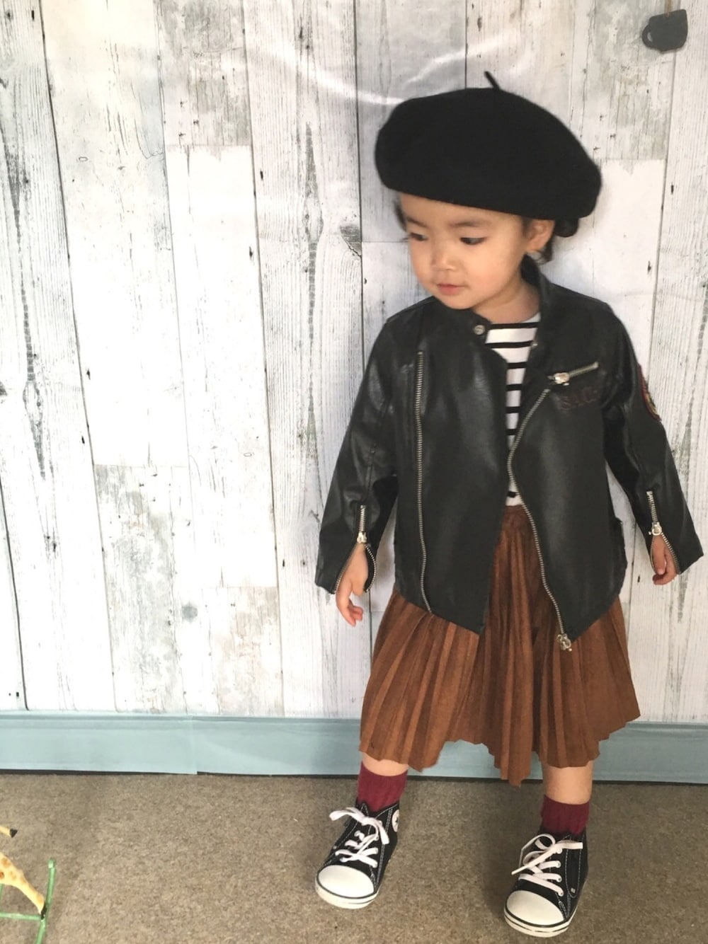 ブラウン系のスカート、ブラック系のスニーカー、ブラック系のライダースジャケットを着用したキッズの春コーディネートの1枚目の写真