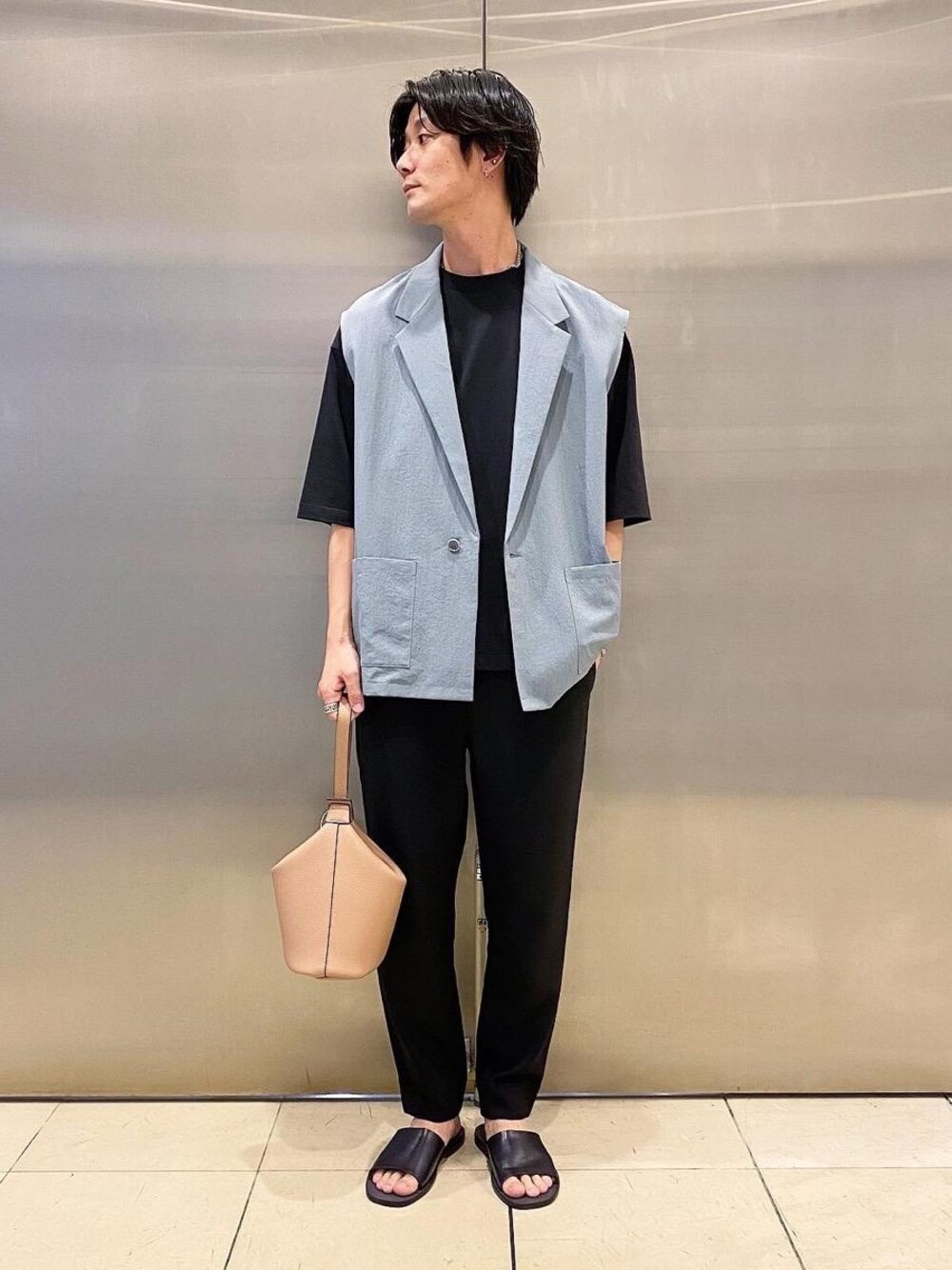 ベージュ系のハンドバッグ、ブルー系のベスト、ブラック系のTシャツ/カットソーを着用したメンズの春コーディネートの1枚目の写真