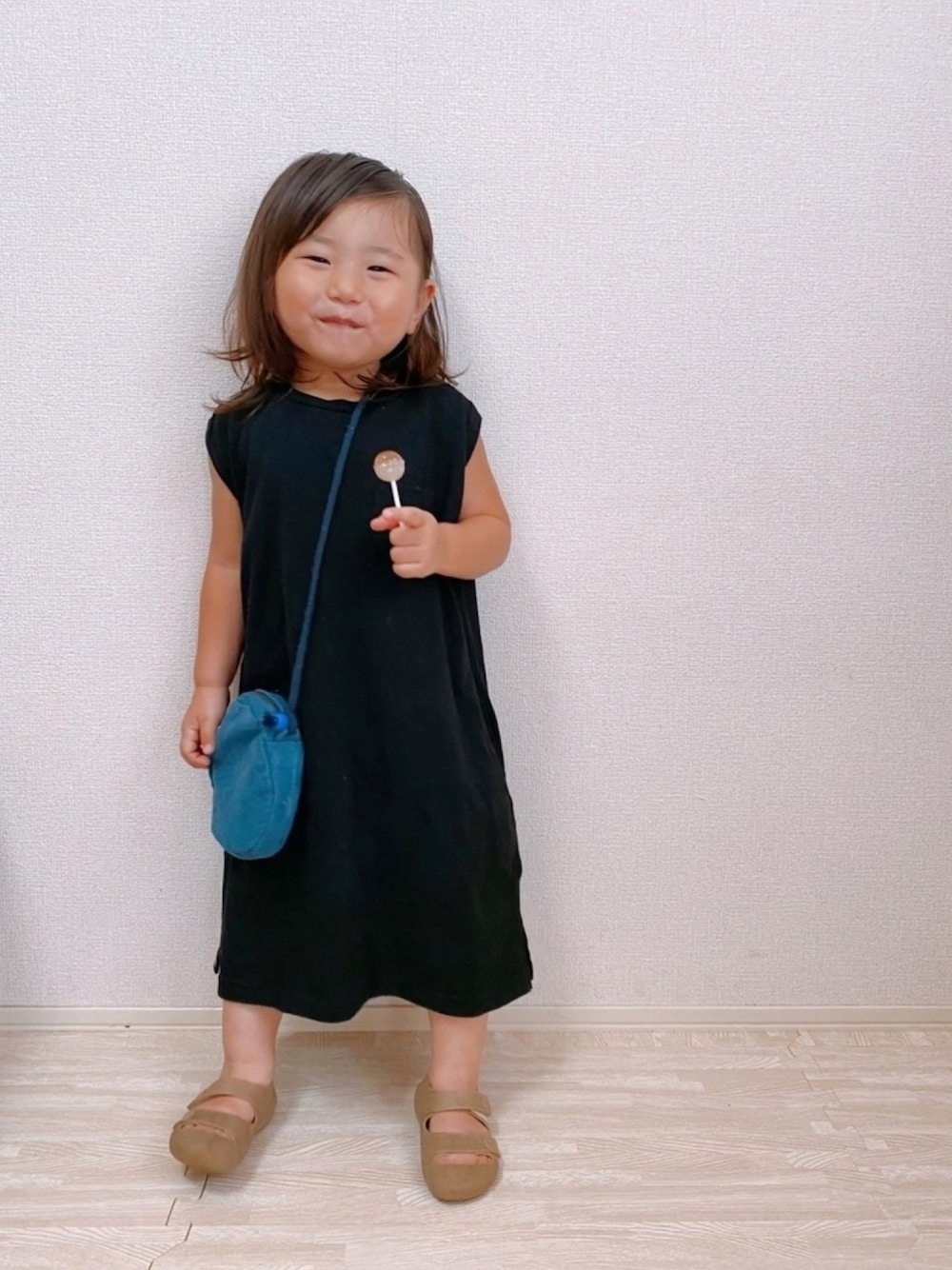 ブラック系のワンピース、ベージュ系のサンダル、ブルー系のショルダーバッグを着用したキッズの夏コーディネートの1枚目の写真