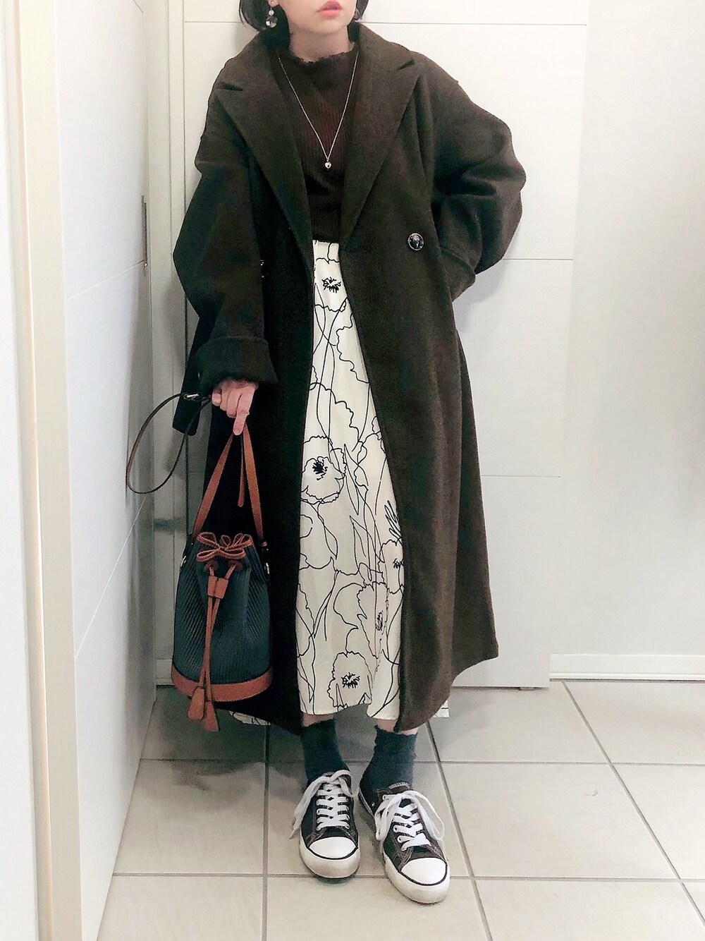 ブラウン系のチェスターコート、ブラウン系のニット/セーター、ホワイト系のスカートを着用したレディースの秋コーディネートの1枚目の写真