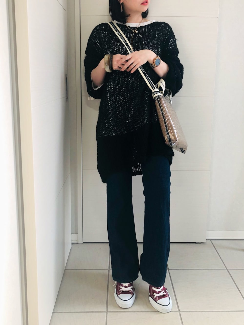 ブラック系のニット/セーター、ブルー系のデニムパンツ、レッド系のスニーカーを着用したレディースの春コーディネートの1枚目の写真