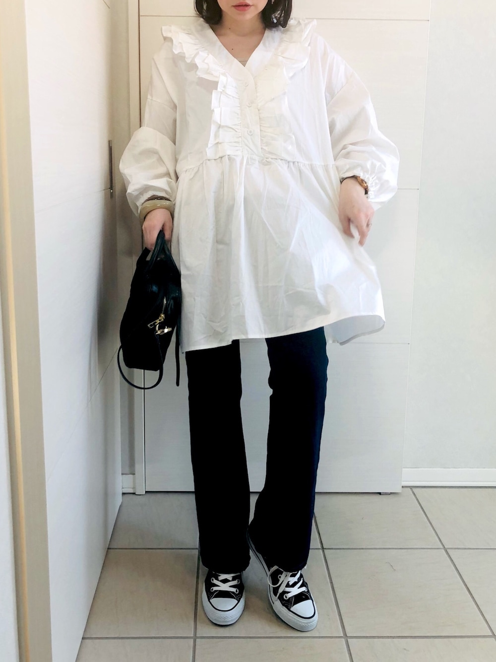 ホワイト系のチュニック、ブルー系のデニムパンツ、ブラック系のスニーカーを着用したレディースの春コーディネートの1枚目の写真