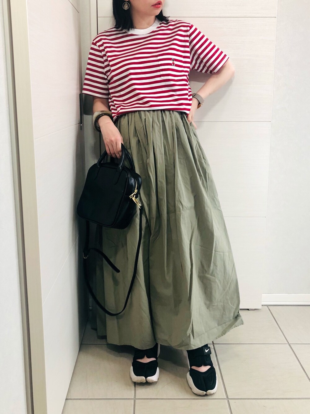 レッド系のTシャツ/カットソー、グリーン系のスカート、ブラック系のスニーカーを着用したレディースの春コーディネートの1枚目の写真