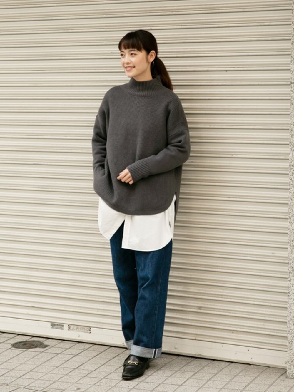 グレー系のニット/セーター、ホワイト系のシャツ/ブラウス、ブルー系のデニムパンツを着用したレディースの冬コーディネートの1枚目の写真