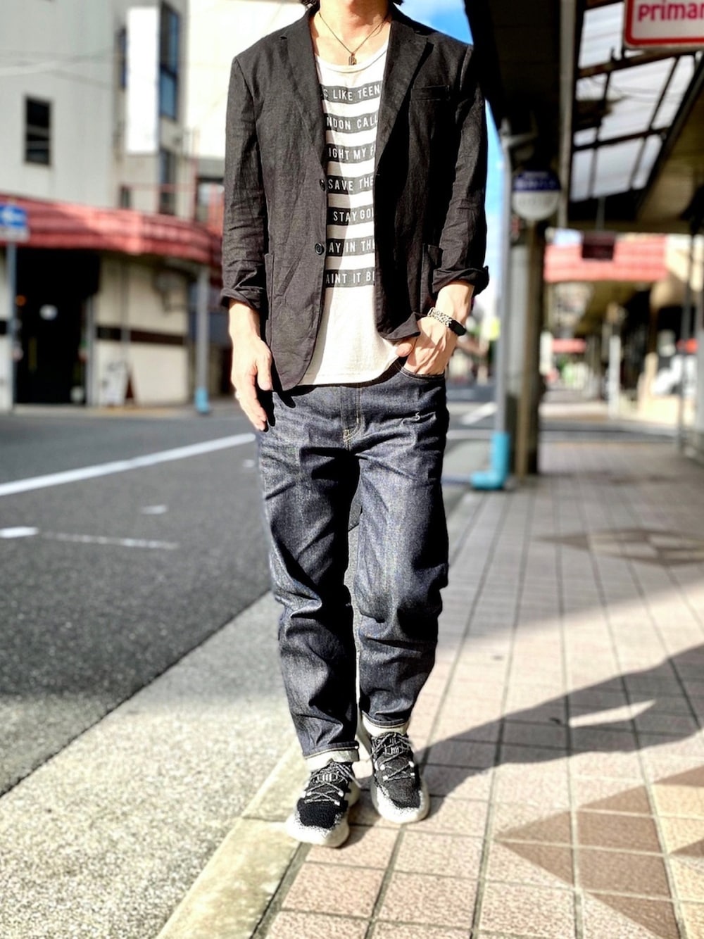 ブラック系のテーラードジャケット、ベージュ系のTシャツ/カットソー、ブルー系のデニムパンツを着用したメンズの秋コーディネートの1枚目の写真