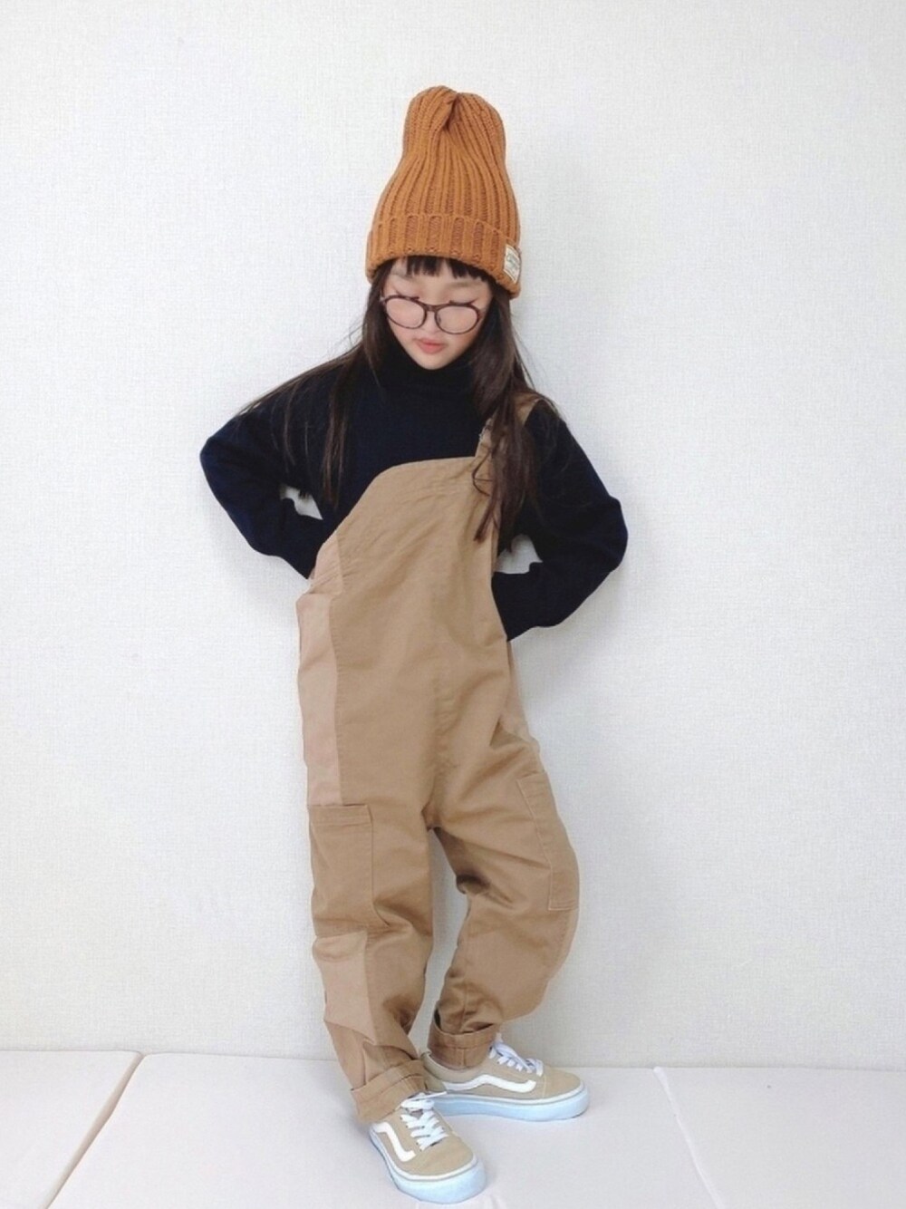 ブラック系のニット/セーター、ベージュ系のサロペット/オーバーオール、ベージュ系のスニーカーを着用したキッズの秋コーディネートの1枚目の写真