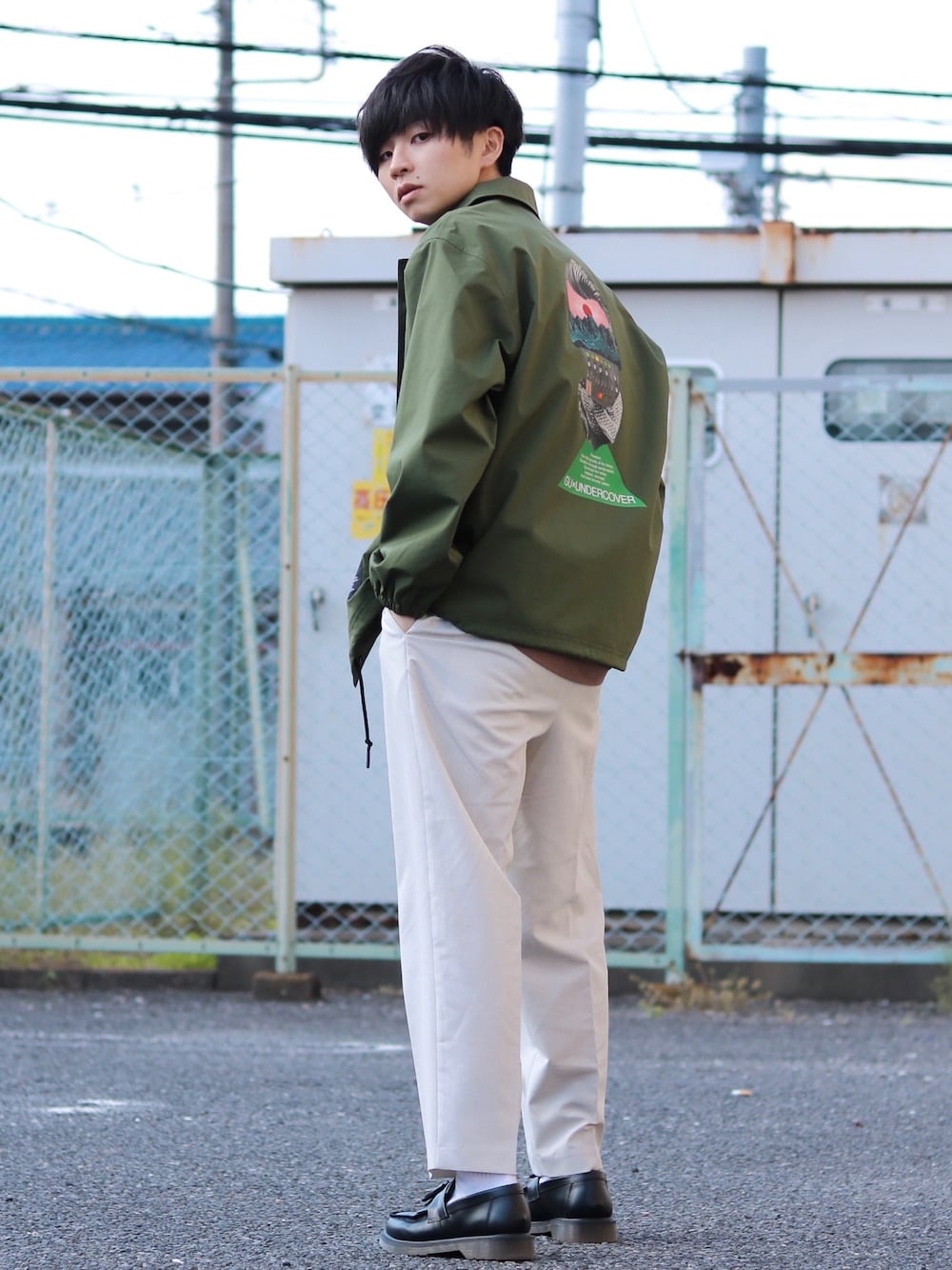 ブラック系のローファー、ホワイト系のスラックス、グリーン系のナイロンジャケットを着用したメンズの春コーディネートの1枚目の写真