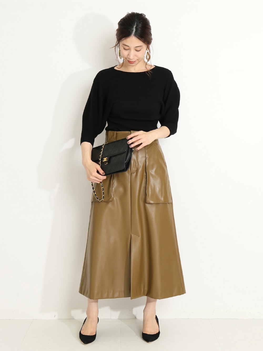 イエロー系のスカート、ブラック系のニット/セーターを着用したレディースの秋コーディネートの1枚目の写真