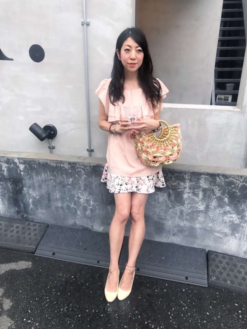 ベージュ系のかごバッグ、ベージュ系のトップス、ゴールド系のチャームを着用したレディースの夏コーディネートの1枚目の写真