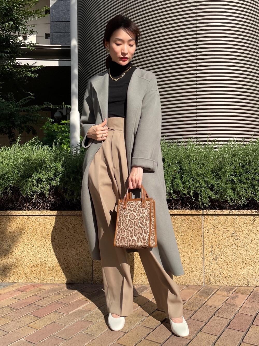 グレー系のノーカラーコート、ベージュ系のハンドバッグ、ブラック系のニット/セーターを着用したレディースの秋コーディネートの1枚目の写真