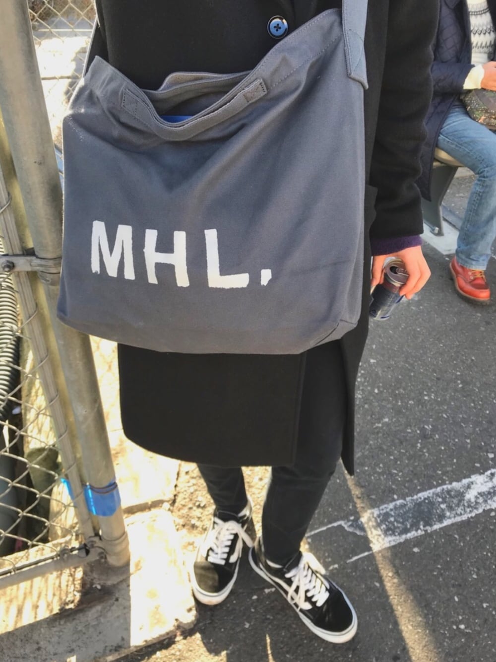 グレー系のトートバッグ、ブラック系のチェスターコート、ブラック系のチノパンツを着用したメンズの冬コーディネートの1枚目の写真