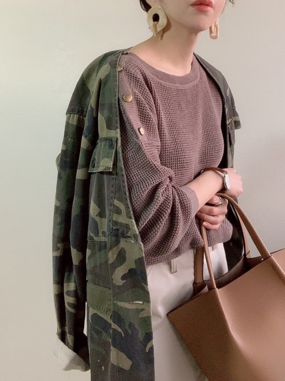 ベージュ系のニット/セーター、イエロー系のバッグ、グリーン系のミリタリージャケットを着用したレディースの春コーディネートの1枚目の写真