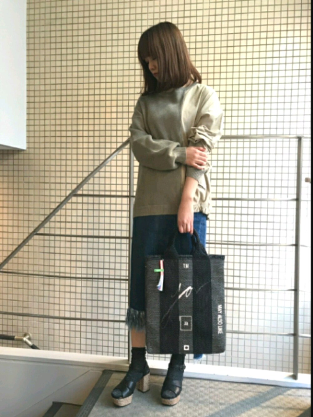 ベージュ系のニット/セーター、ブルー系のスカート、ブラック系のトートバッグを着用したレディースの春コーディネートの1枚目の写真