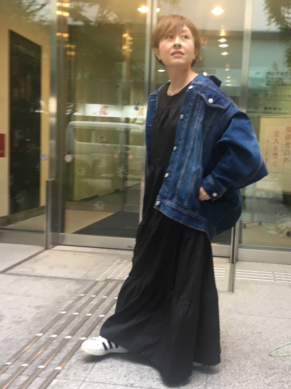 ブルー系のデニムジャケット、ブラック系のワンピース、ホワイト系のスニーカーを着用したレディースの春コーディネートの1枚目の写真