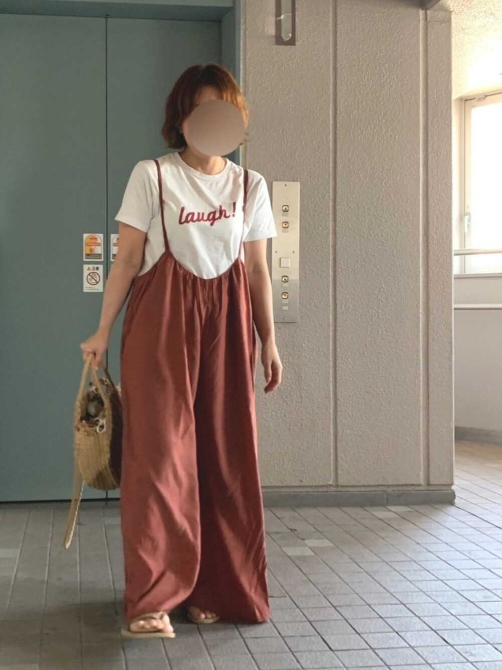 レッド系のオールインワン・サロペット、ベージュ系のかごバッグ、ゴールド系のサンダルを着用したレディースの春コーディネートの1枚目の写真