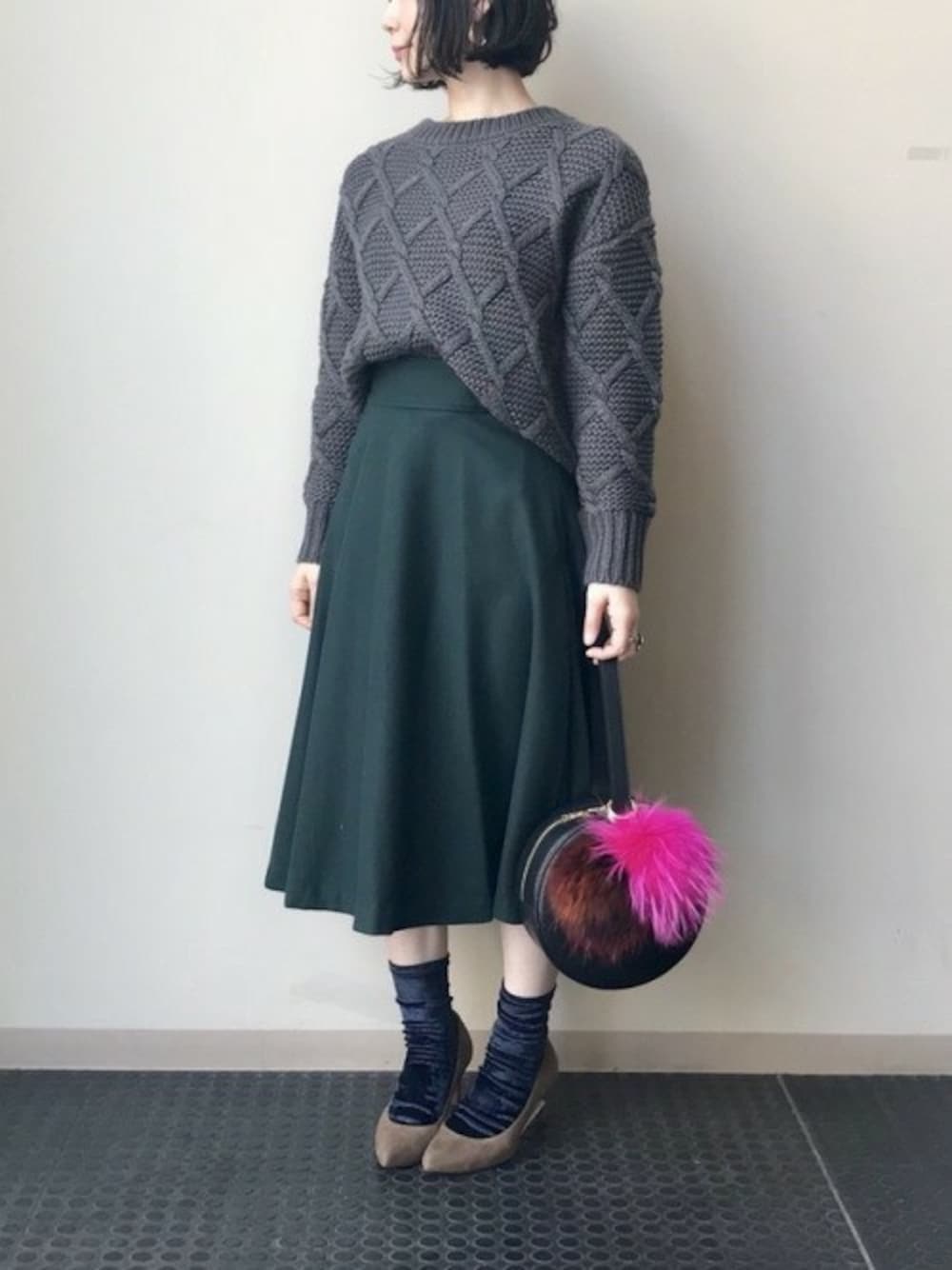 グレー系のニット/セーター、グリーン系のスカート、ブラック系のショルダーバッグを着用したレディースの秋コーディネートの1枚目の写真