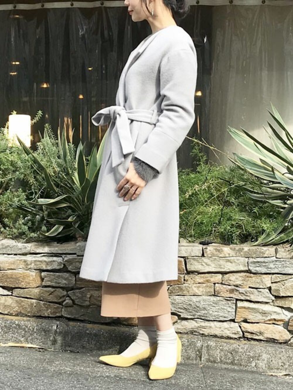 グレー系のノーカラーコート、グレー系のニット/セーター、ベージュ系のスカートを着用したレディースの秋コーディネートの1枚目の写真