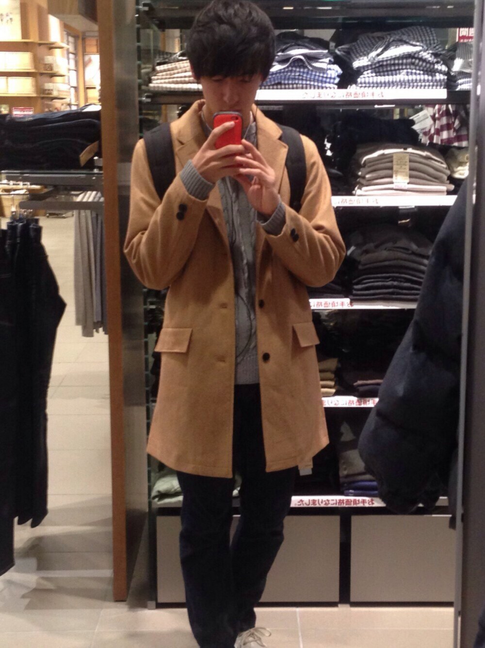 ブラック系のバックパック/リュック、ブルー系のデニムパンツ、ベージュ系のチェスターコートを着用したメンズの秋コーディネートの1枚目の写真