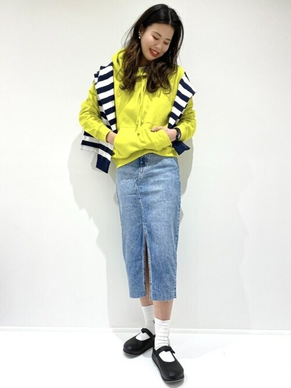イエロー系のパーカー、ブルー系のデニムスカートを着用したレディースの春コーディネートの1枚目の写真