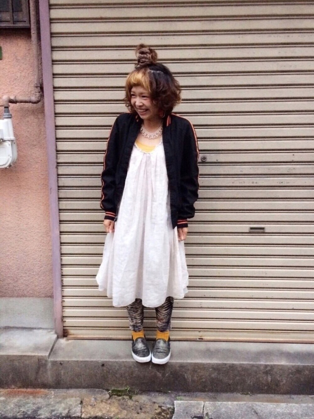 ホワイト系のワンピース、ブラック系のブルゾン、ゴールド系のスニーカーを着用したレディースの春コーディネートの1枚目の写真