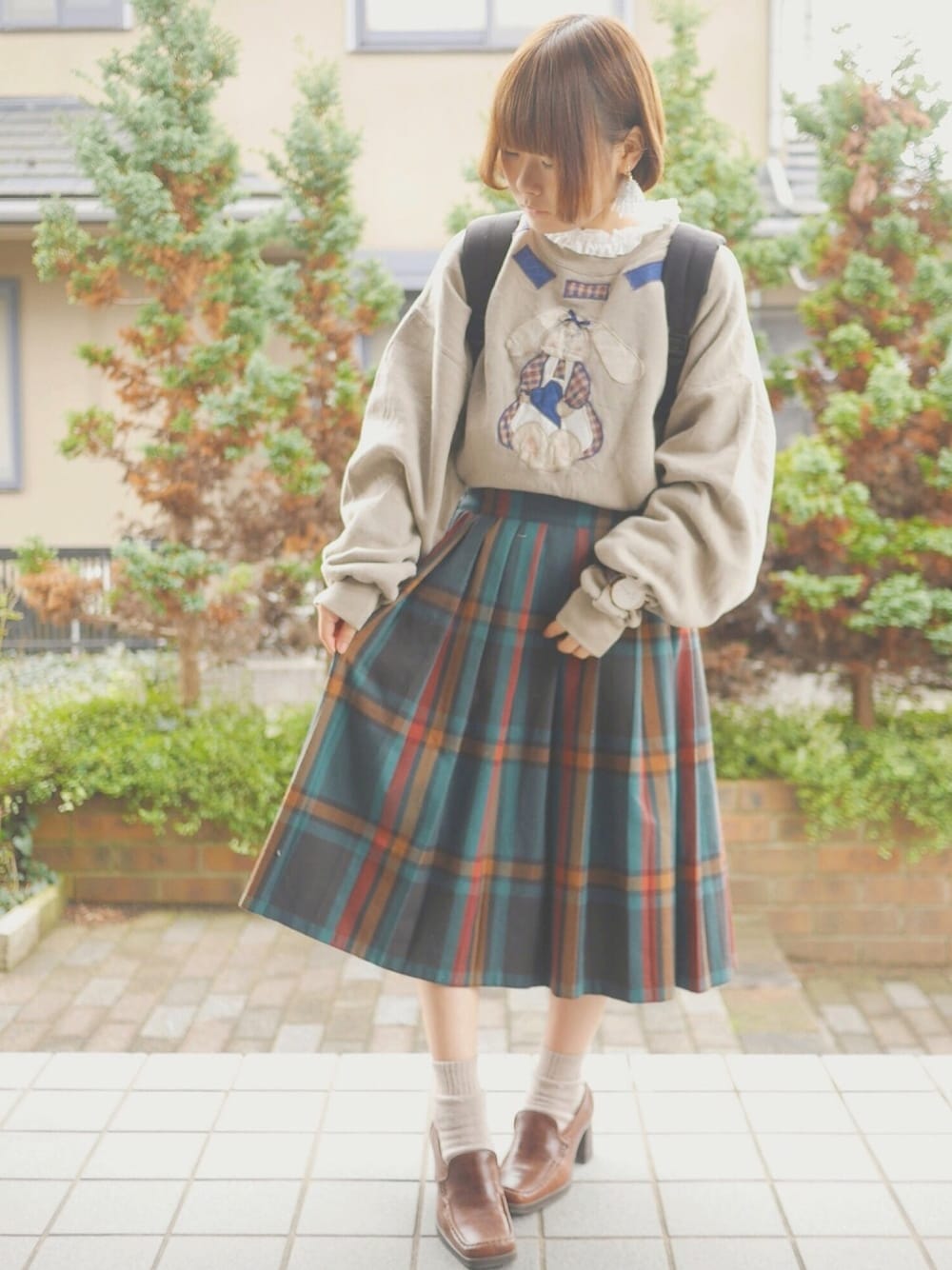 ベージュ系のスウェット、ブラック系のバックパック/リュック、グリーン系のスカートを着用したレディースの冬コーディネートの1枚目の写真