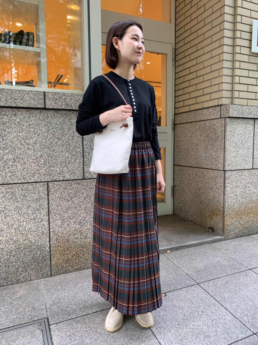 ブラウン系のスカート、ホワイト系のショルダーバッグ、ブラック系のTシャツ/カットソーを着用したレディースの秋コーディネートの1枚目の写真