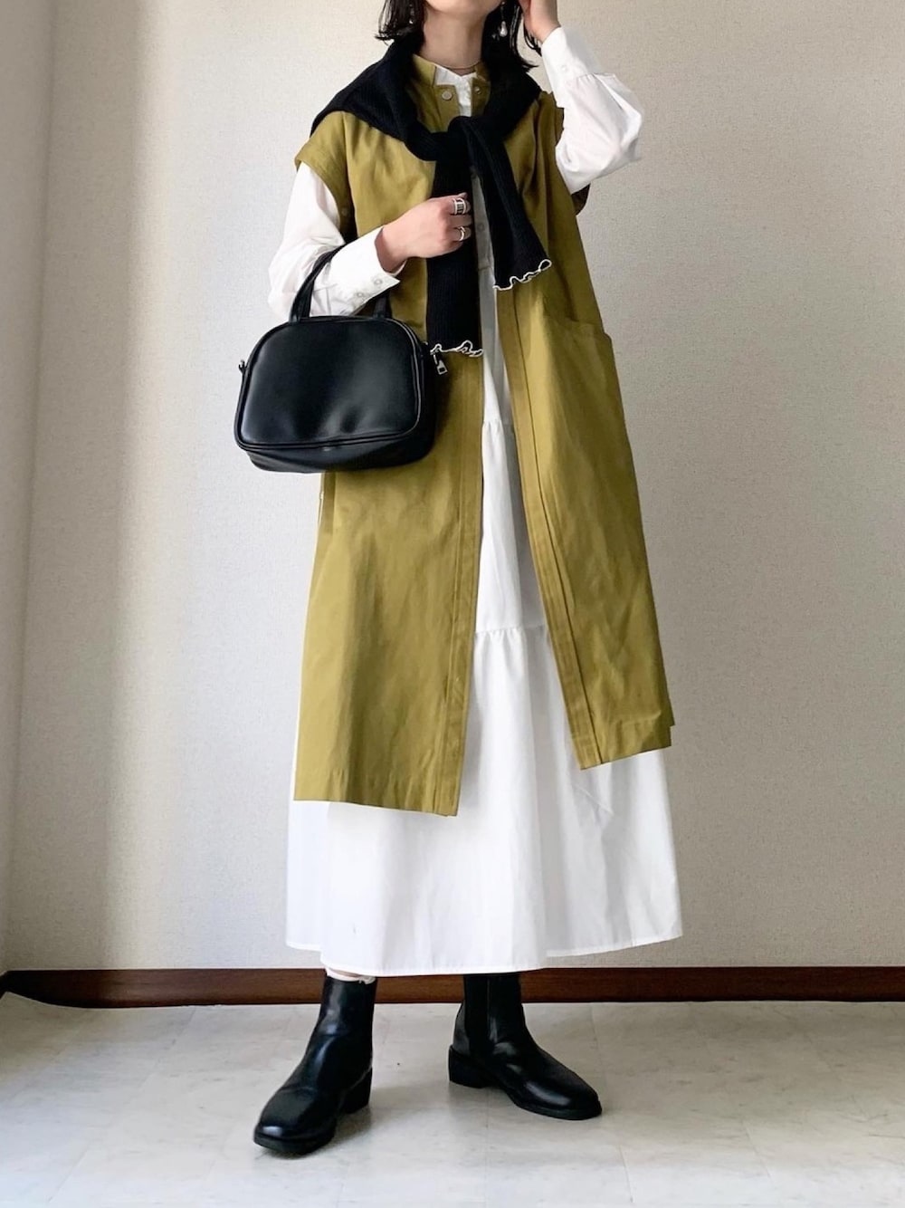 イエロー系のノーカラーコート、ブラック系のカーディガン/ボレロ、ホワイト系のシャツワンピースを着用したレディースの春コーディネートの1枚目の写真