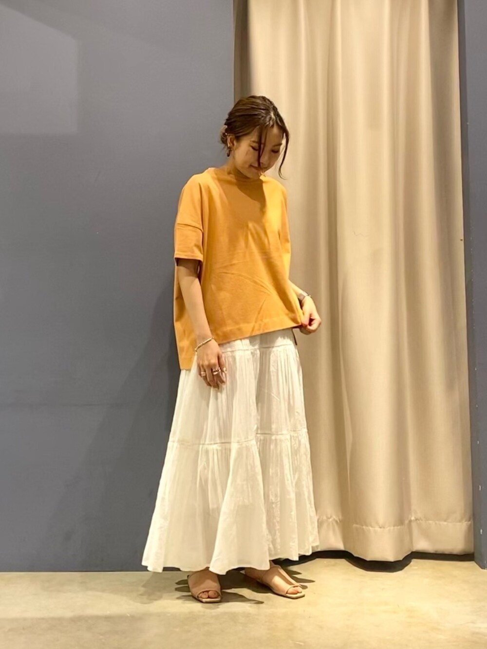 オレンジ系のTシャツ/カットソー、ホワイト系のスカート、ベージュ系のサンダルを着用したレディースの春コーディネートの1枚目の写真