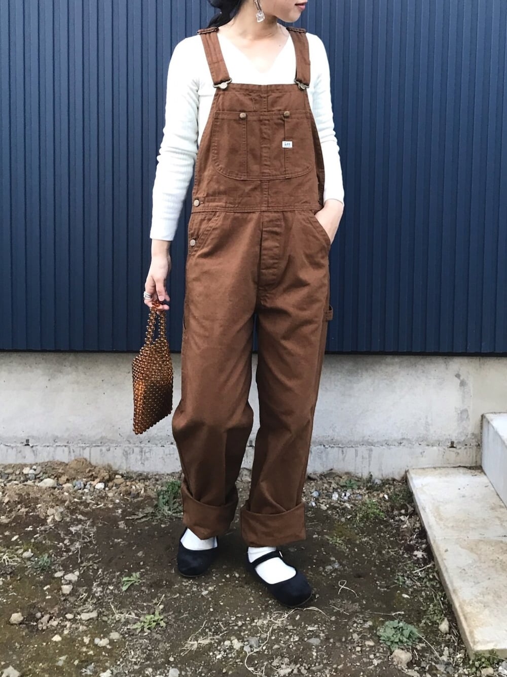 ブラウン系のサロペット/オーバーオール、ホワイト系のニット/セーター、ブラック系のバレエシューズを着用したレディースの春コーディネートの1枚目の写真