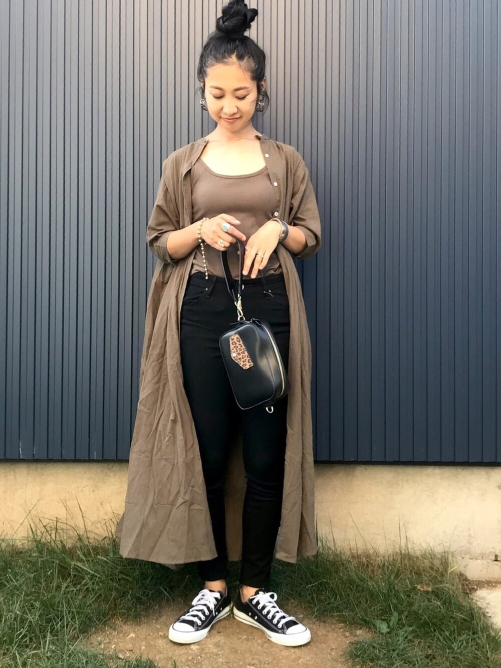 グリーン系のワンピース、ブラック系のデニムパンツ、ブラック系のスニーカーを着用したレディースの秋コーディネートの1枚目の写真