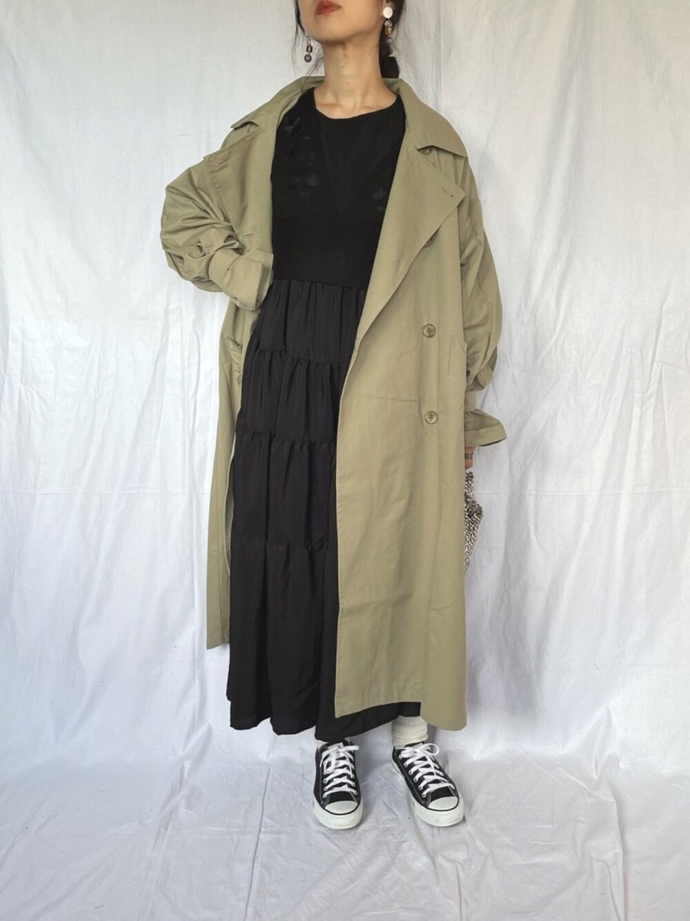 グリーン系のトレンチコート、ブラック系のベスト、ブラック系のワンピースを着用したレディースの冬コーディネートの1枚目の写真