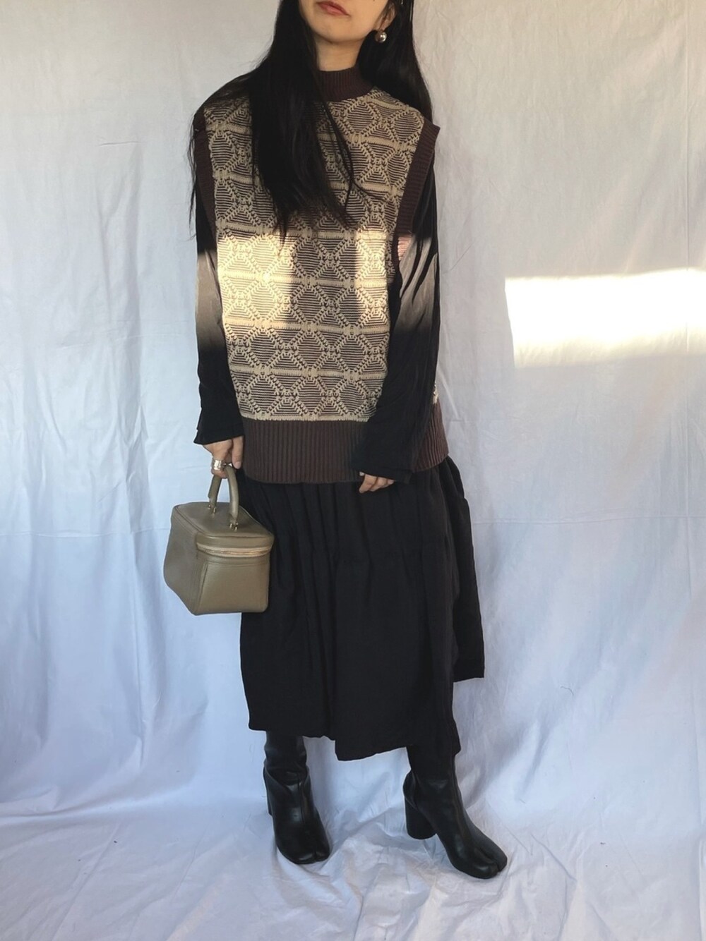 ブラウン系のベスト、ブラック系のワンピースを着用したレディースの冬コーディネートの1枚目の写真