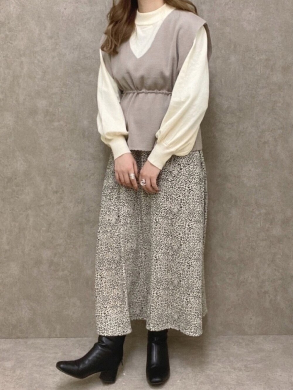 グレー系のベスト、ホワイト系のスカート、ブラック系のブーツを着用したレディースの冬コーディネートの1枚目の写真
