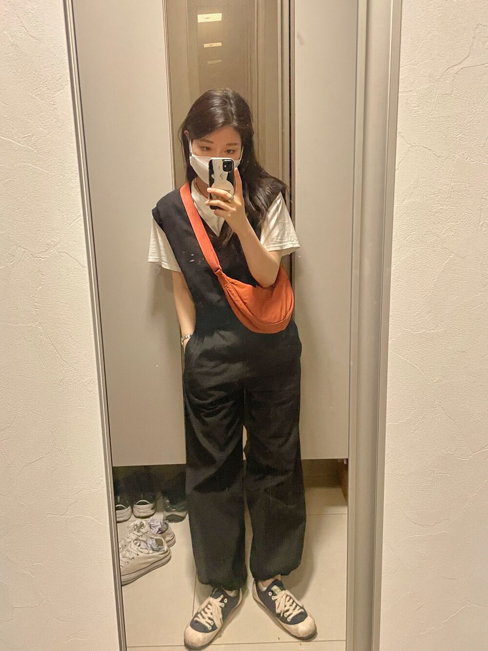 オレンジ系のショルダーバッグ、ブラック系のベスト、ブラック系のチノパンツを着用したレディースの夏コーディネートの1枚目の写真