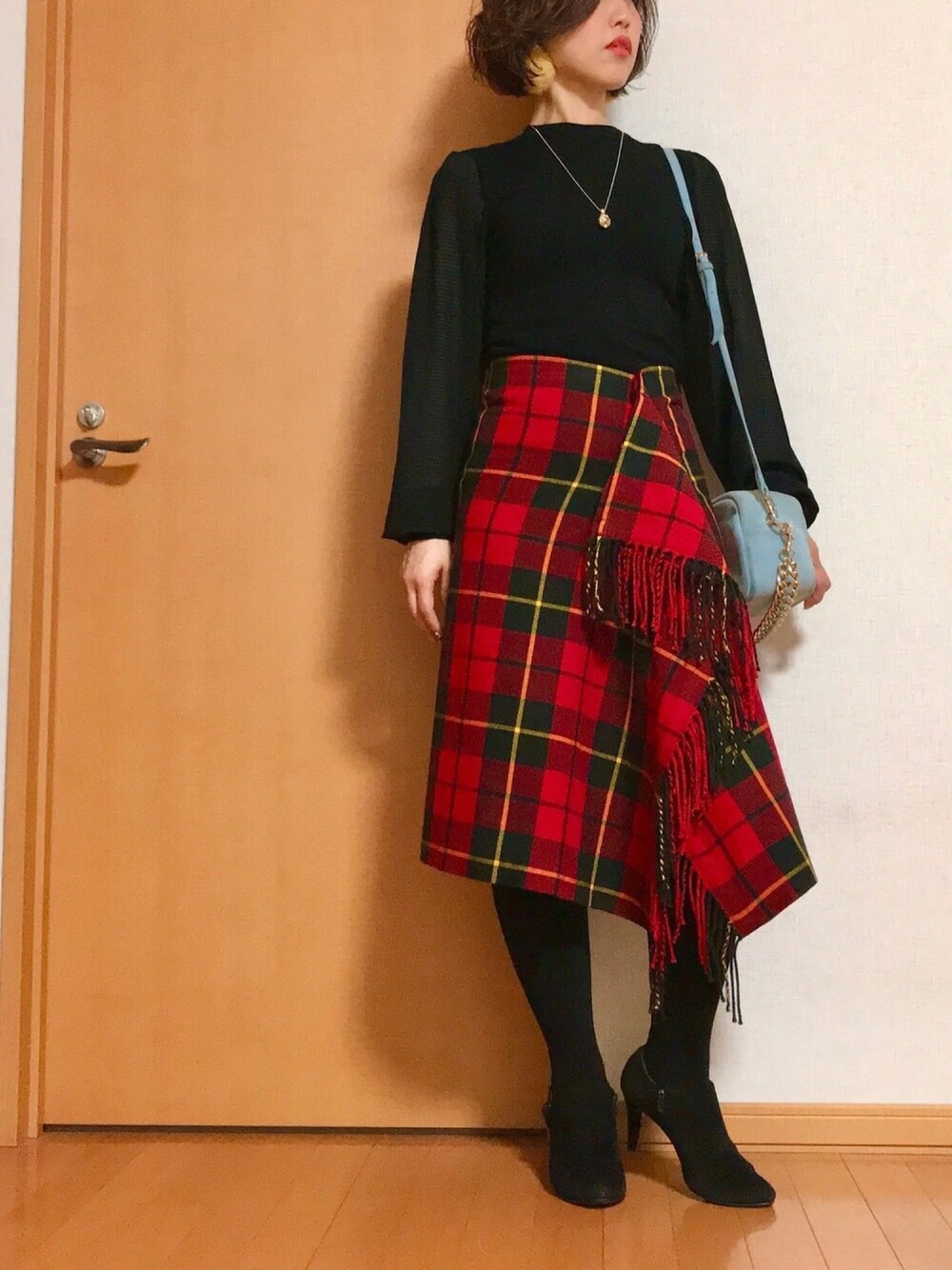 レッド系のスカート、ブラック系のブーティ、ブルー系のショルダーバッグを着用したレディースの冬コーディネートの1枚目の写真