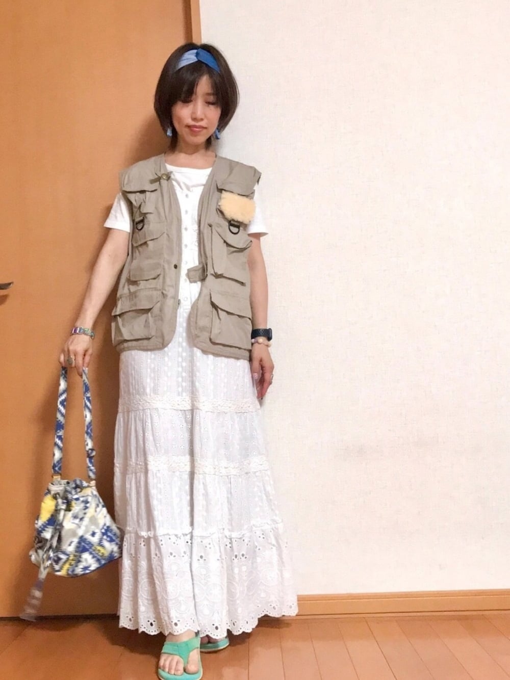 ベージュ系のベスト、ブルー系のショルダーバッグ、ホワイト系のジャンパースカートを着用したレディースの夏コーディネートの1枚目の写真