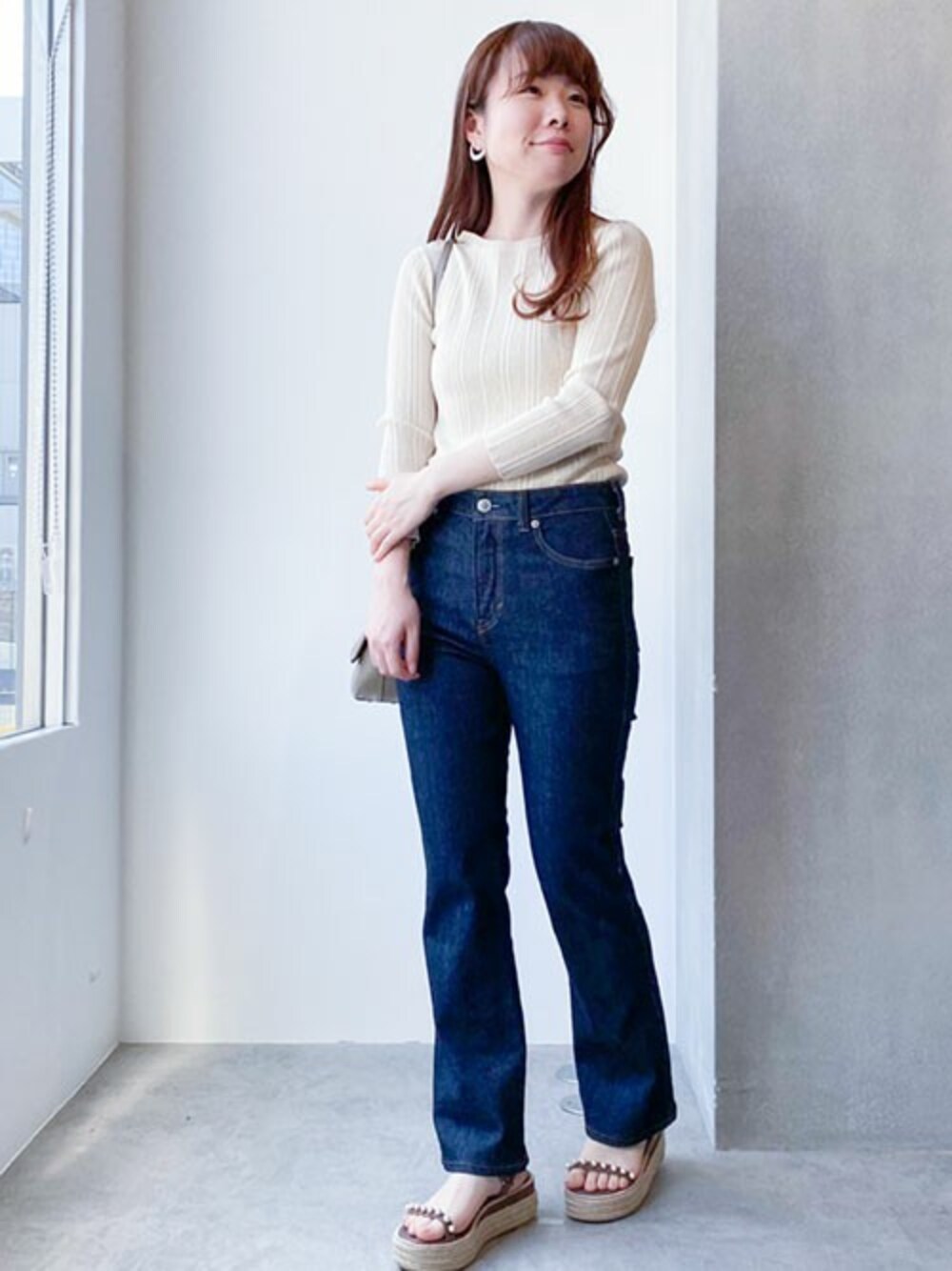 ベージュ系のニット/セーター、ブルー系のデニムパンツ、ベージュ系のショルダーバッグを着用したレディースの春コーディネートの1枚目の写真