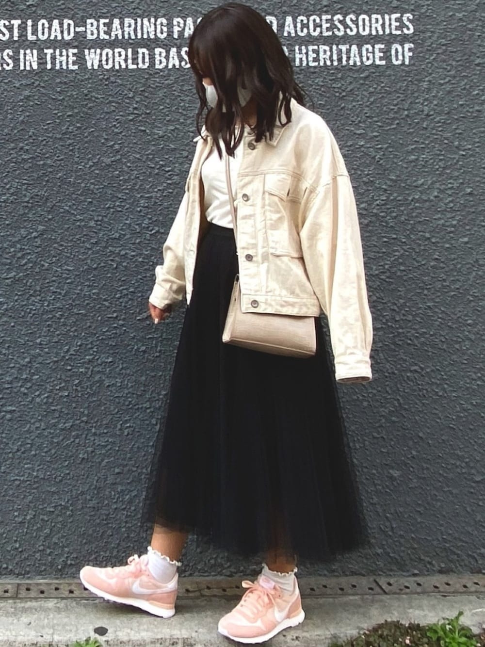 ピンク系のスニーカー、ブラック系のスカート、ホワイト系のデニムジャケットを着用したレディースの春コーディネートの1枚目の写真