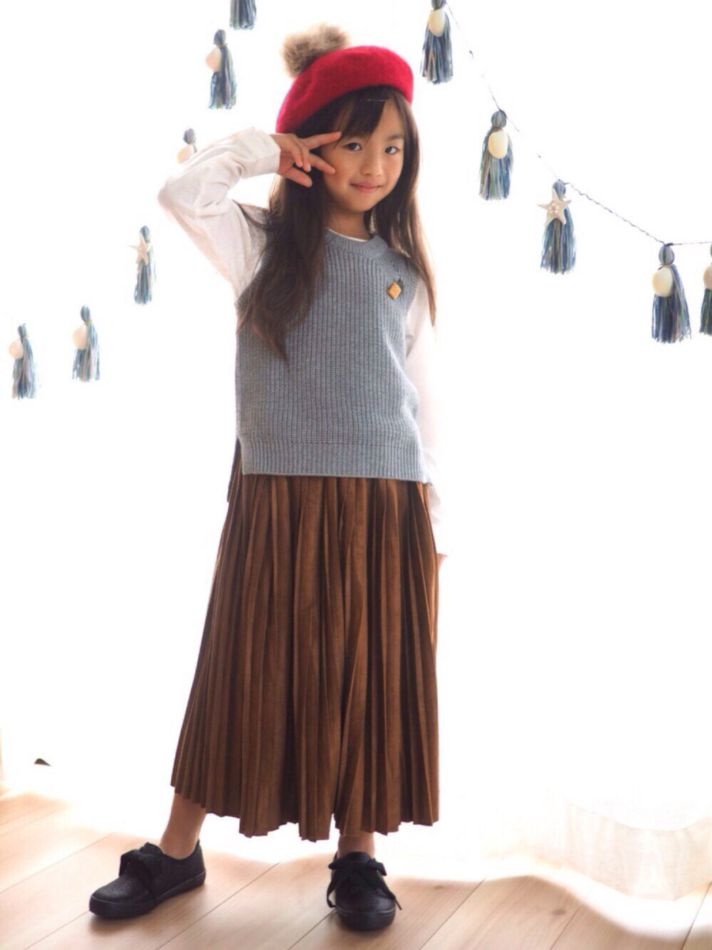 グレー系のベスト、ホワイト系のTシャツ/カットソー、ブラウン系のスカートを着用したキッズの秋コーディネートの1枚目の写真