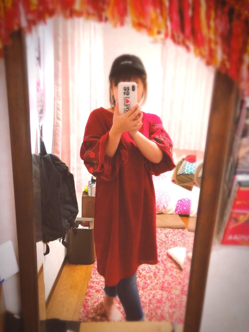 レッド系のワンピース、ブルー系のデニムパンツ、ブラック系のキャップを着用したレディースの秋コーディネートの1枚目の写真