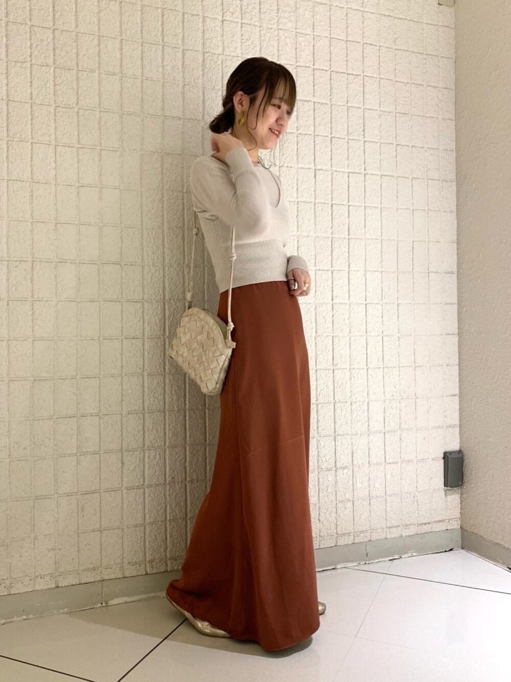 ベージュ系のニット/セーター、ブラウン系のスカート、ホワイト系のショルダーバッグを着用したレディースの春コーディネートの1枚目の写真