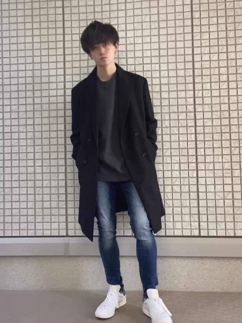 グレー系のニット/セーター、ブラック系のチェスターコート、グリーン系のスニーカーを着用したメンズの冬コーディネートの1枚目の写真