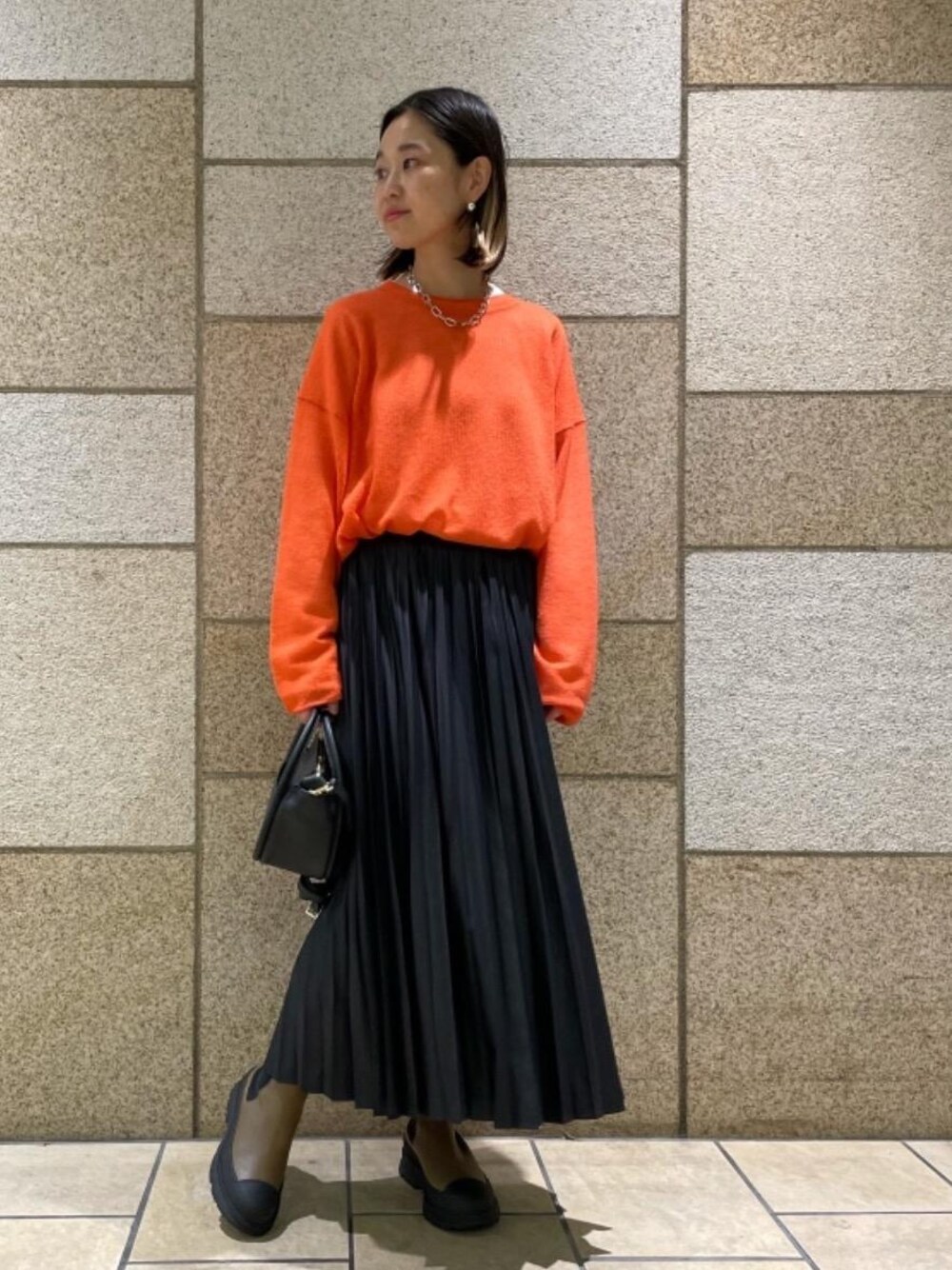 ホワイト系のTシャツ/カットソー、ブラック系のスカート、オレンジ系のニット/セーターを着用したレディースの秋コーディネートの1枚目の写真