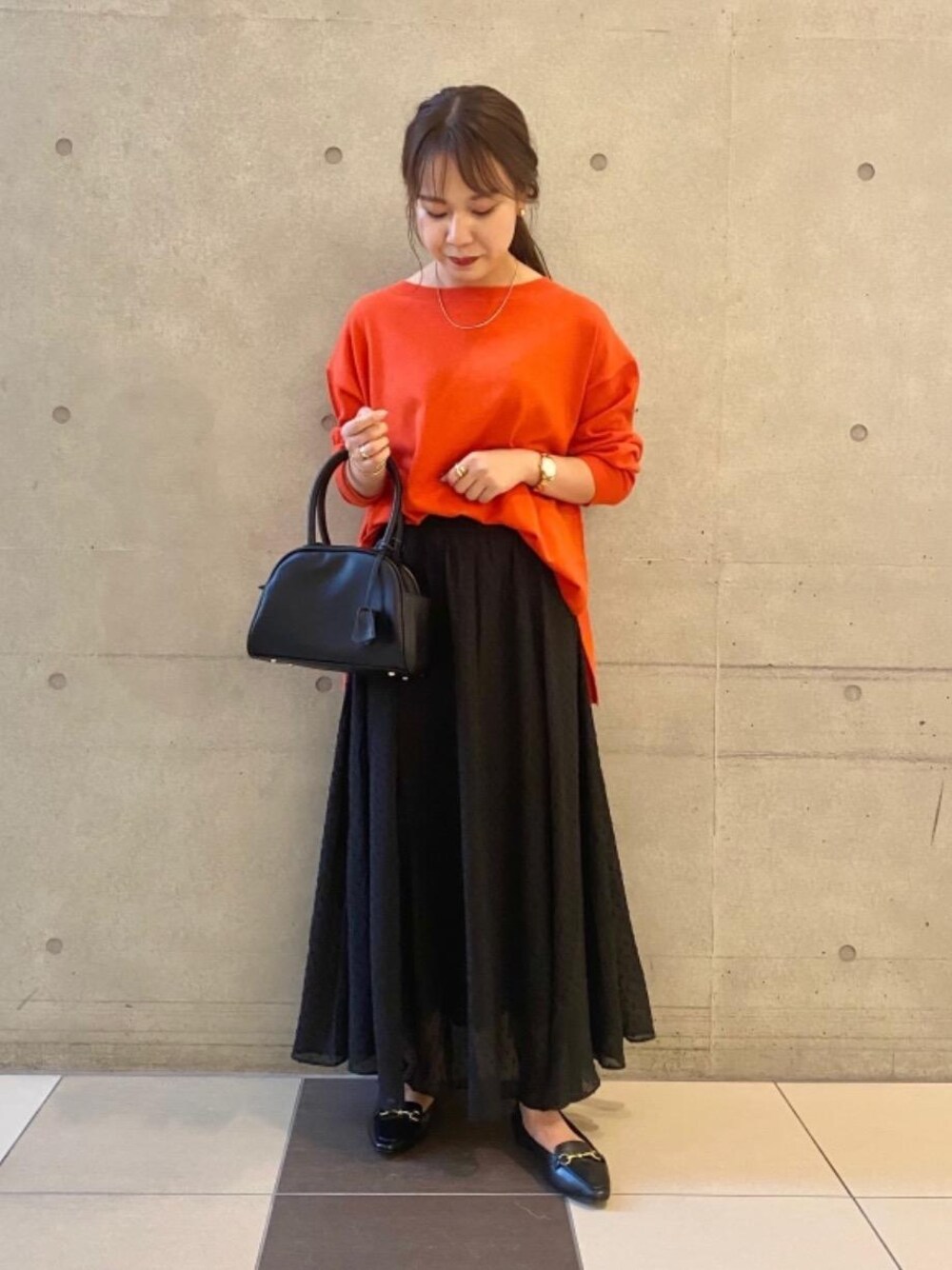 ブラック系のショルダーバッグ、ブラック系のスカート、オレンジ系のニット/セーターを着用したレディースの夏コーディネートの1枚目の写真