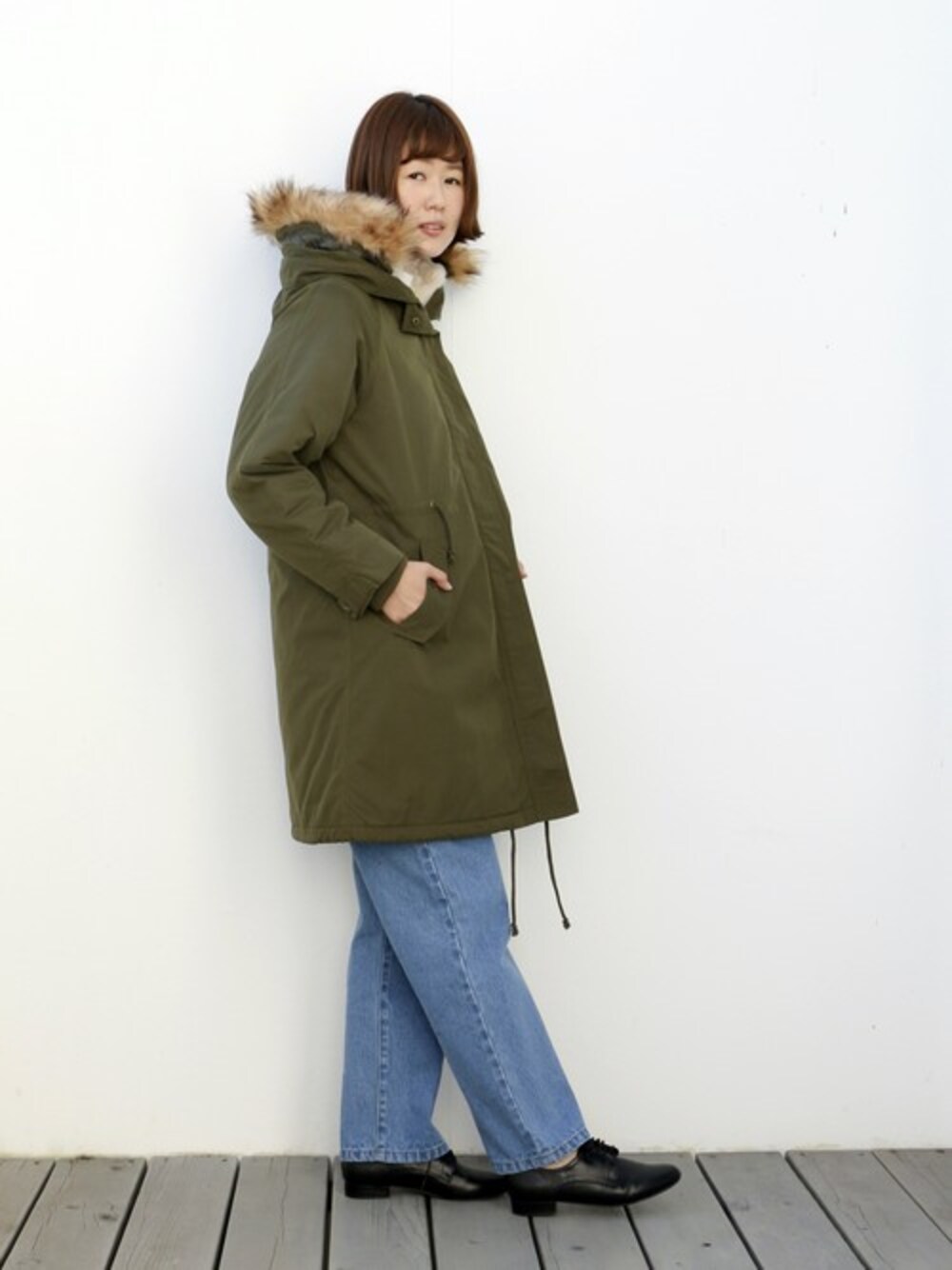 グリーン系のモッズコート、ブルー系のデニムパンツ、ブラック系のドレスシューズを着用したレディースの冬コーディネートの1枚目の写真