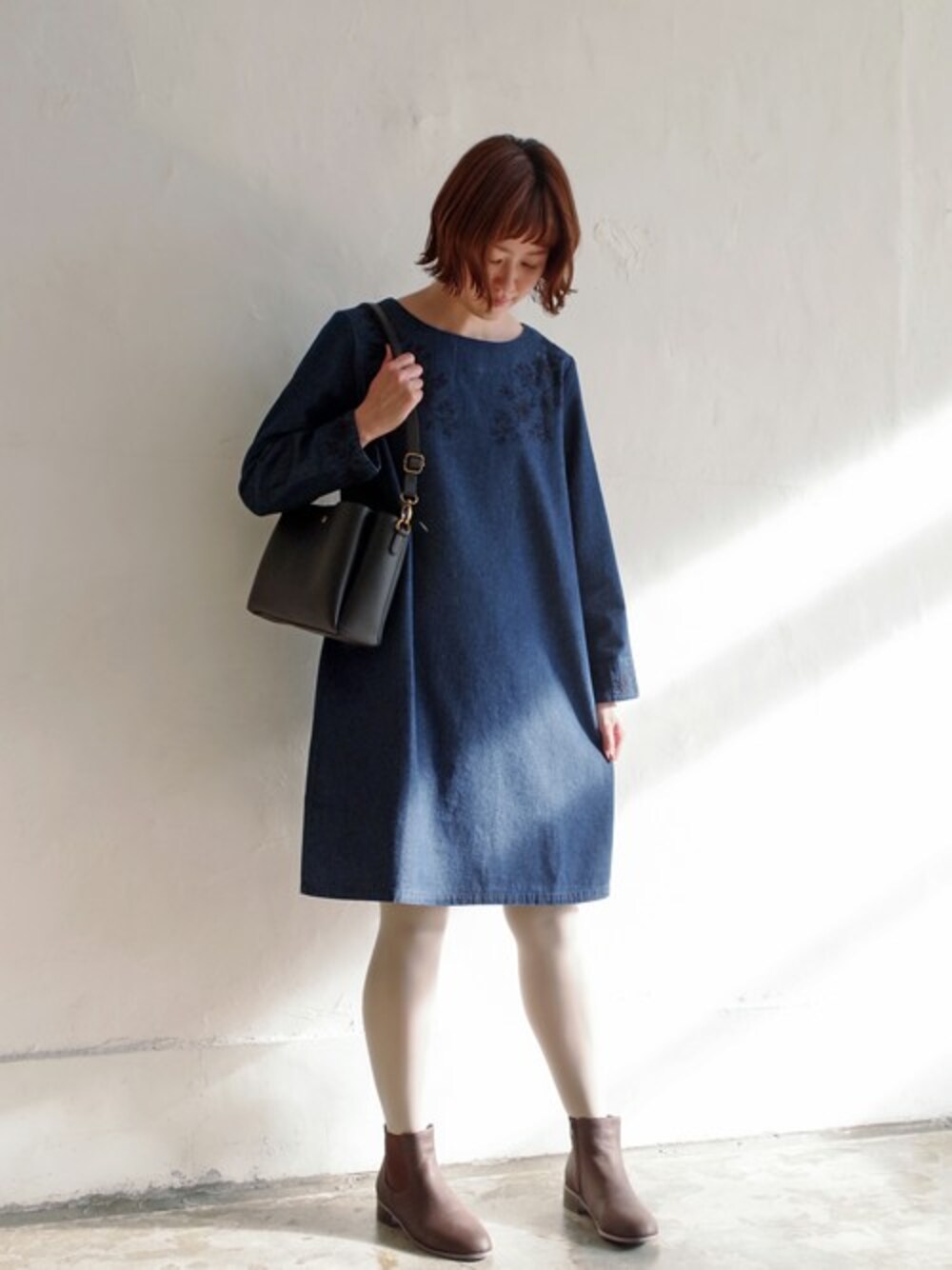ブルー系のワンピース、ブラック系のショルダーバッグ、ブラウン系のブーツを着用したレディースの冬コーディネートの1枚目の写真