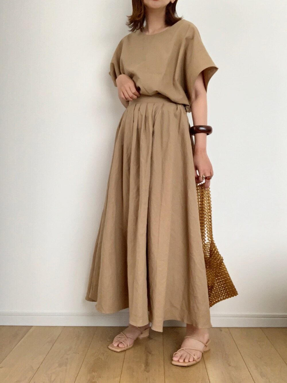 ベージュ系のスカート、ベージュ系のサンダル、ブラウン系のトートバッグを着用したレディースの夏コーディネートの1枚目の写真