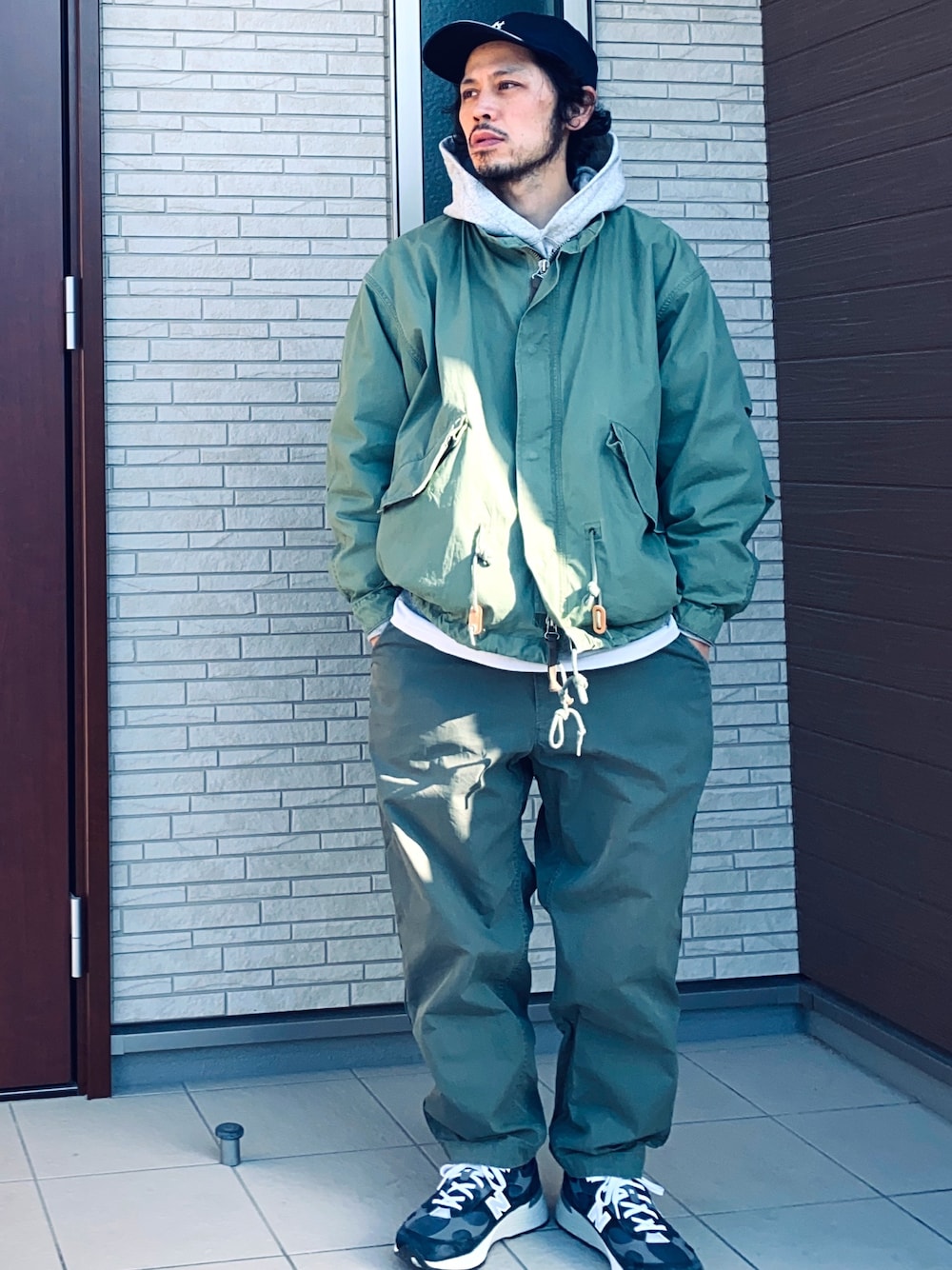 グレー系のパーカー、グリーン系のパンツ、ブルー系のスニーカーを着用したメンズの冬コーディネートの1枚目の写真