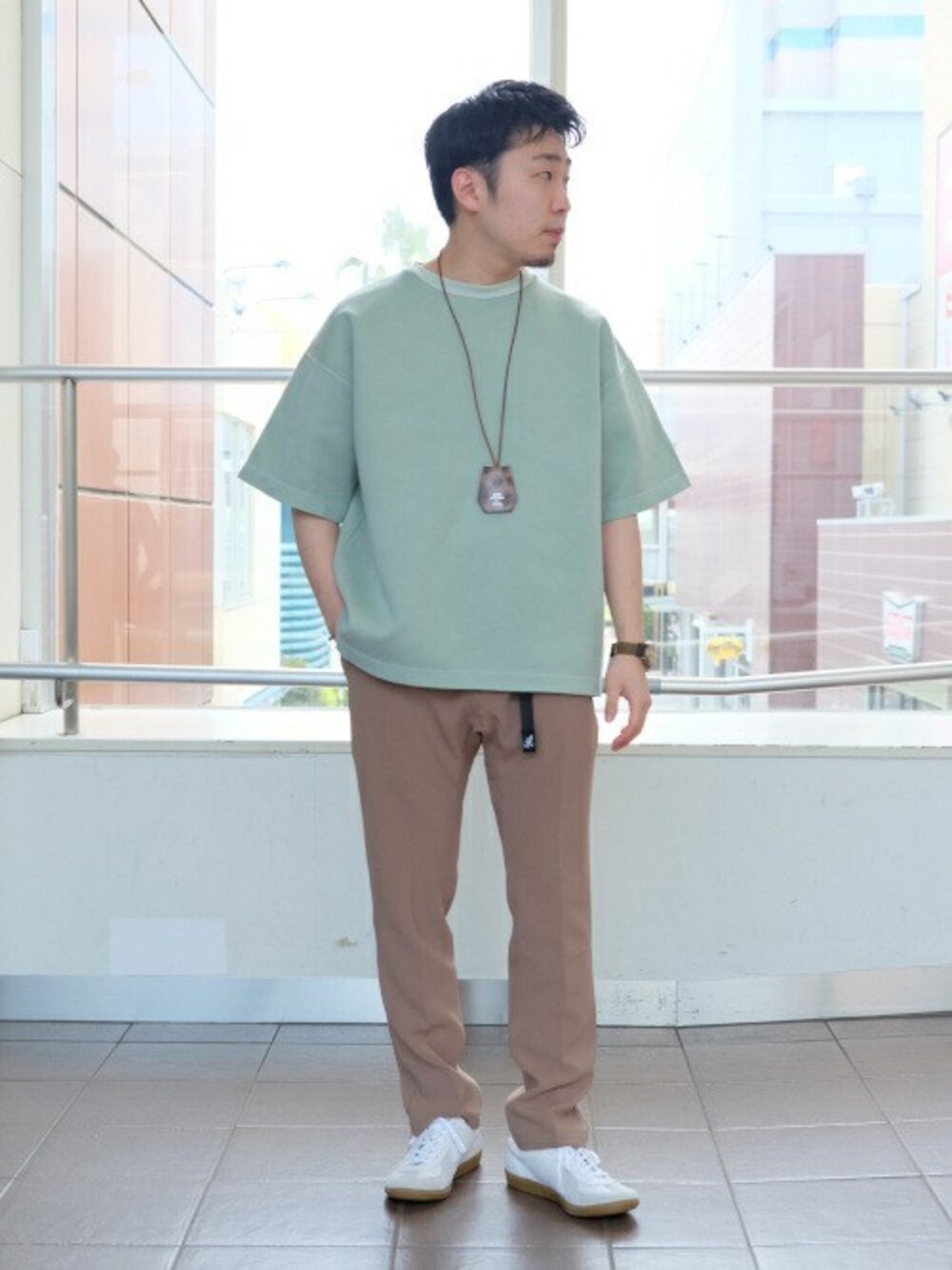 グリーン系のTシャツ/カットソー、ベージュ系のスラックス、ホワイト系のスニーカーを着用したメンズの春コーディネートの1枚目の写真